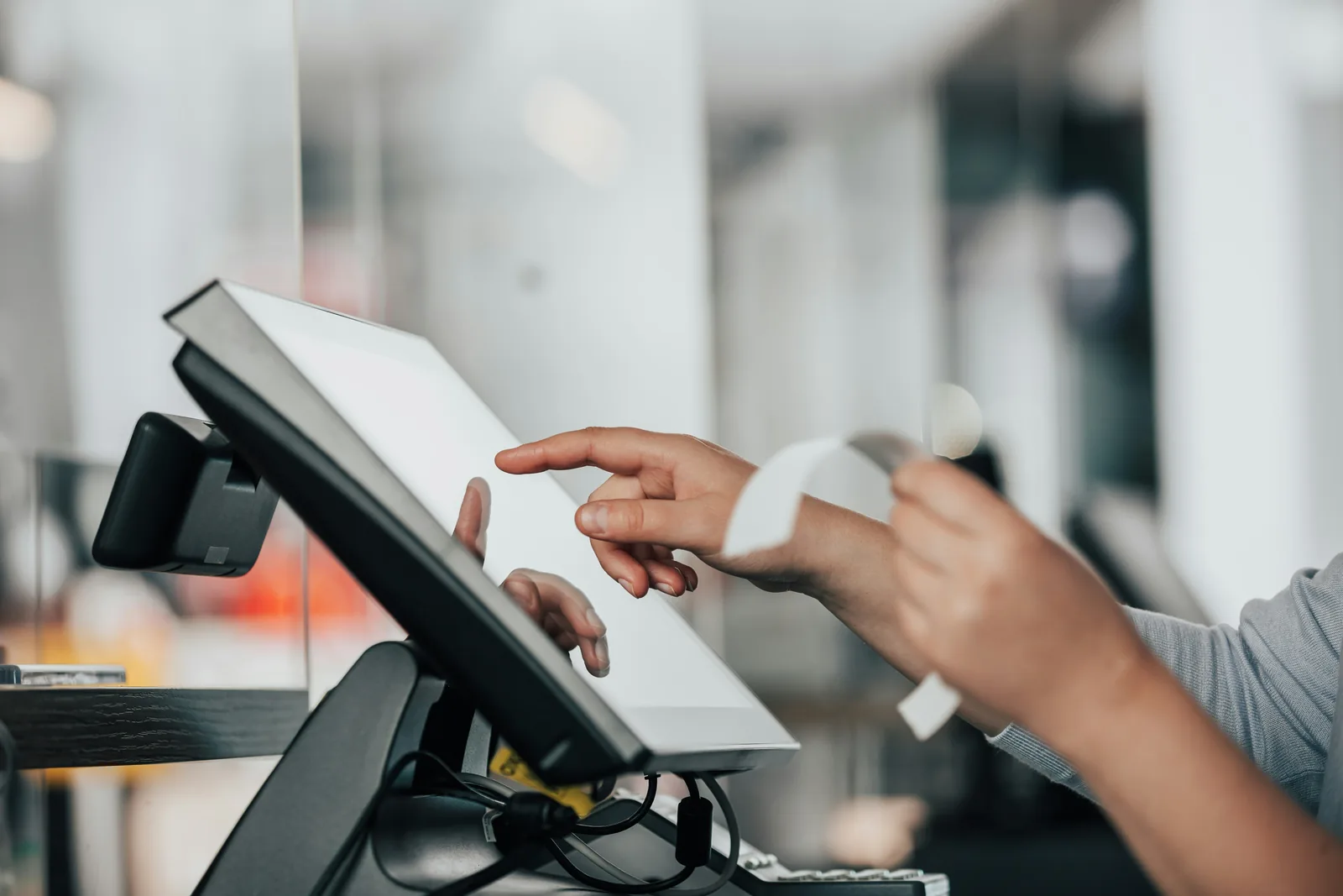 Hands using a touchscreen till system at a counter and tearing off a printed receipt