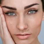 A close-up of a woman’s face with microblading on her brows and natural make-up with dark hair tied up