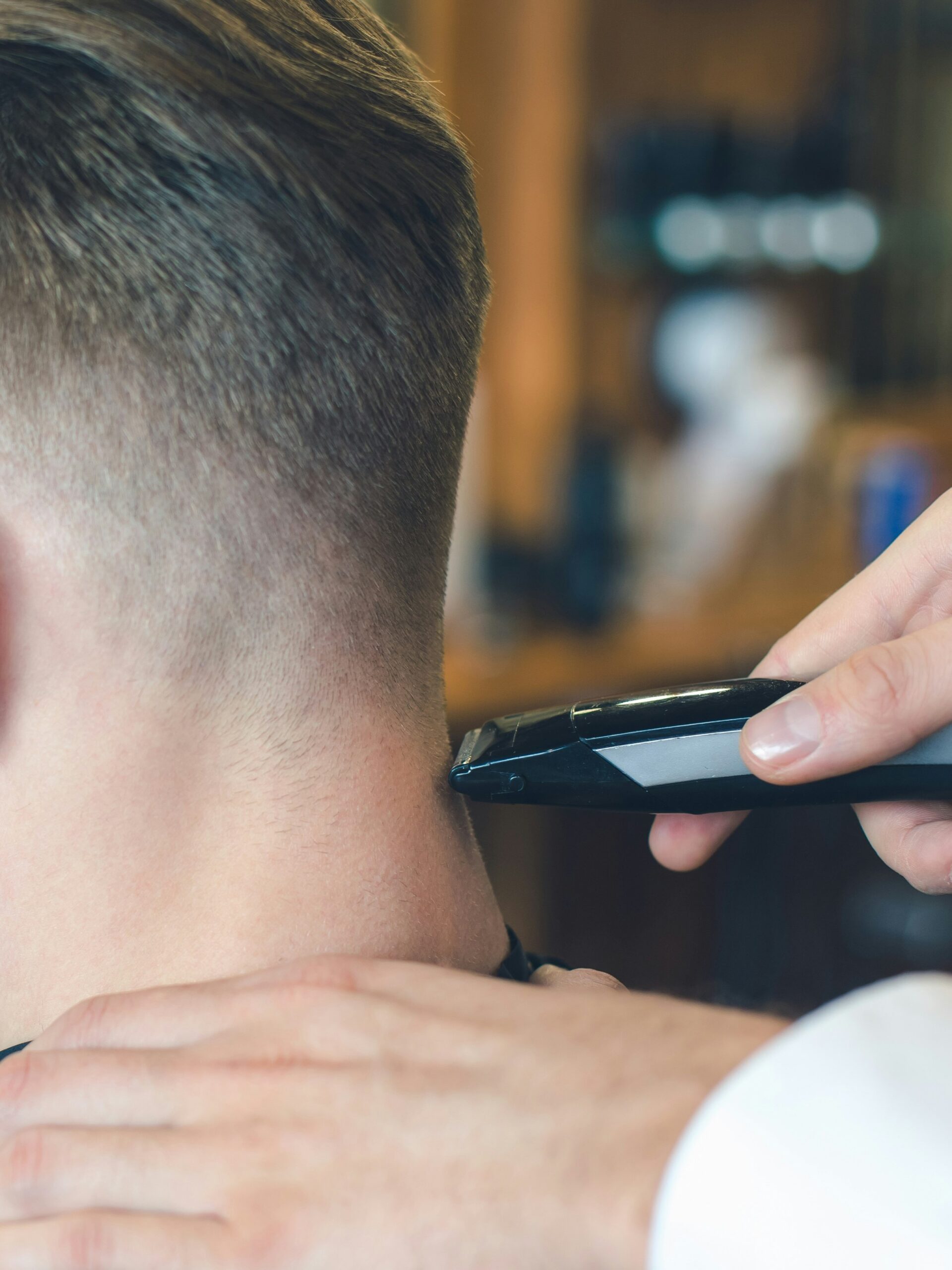 Close-up of a barber cutting a taper fade for a client with straight hair using clippers at the back of the head