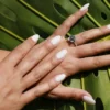Studio shot of fresh almond-shaped nude-colour acrylic nails on a palm leaf backdrop