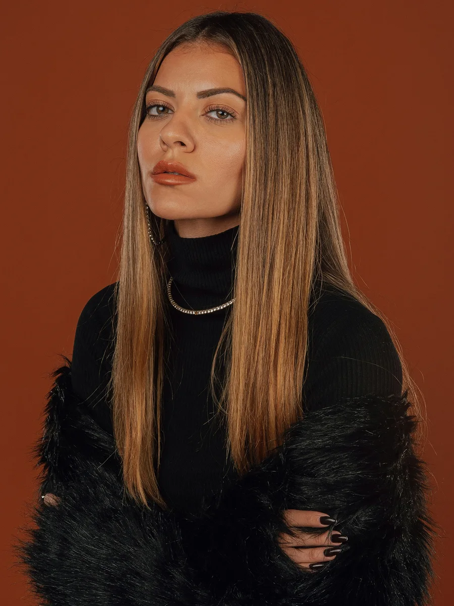 Studio portrait of a woman with long, glossy medium-brown hair wearing a black top, black fur wrap and sparkly hoops and necklace