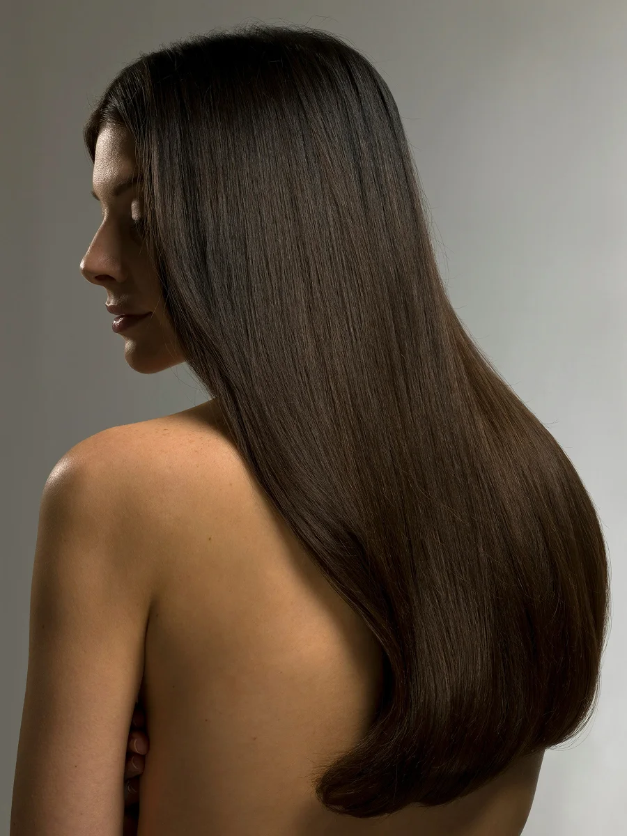 Side view studio portrait of a woman with long, glossy brunette hair