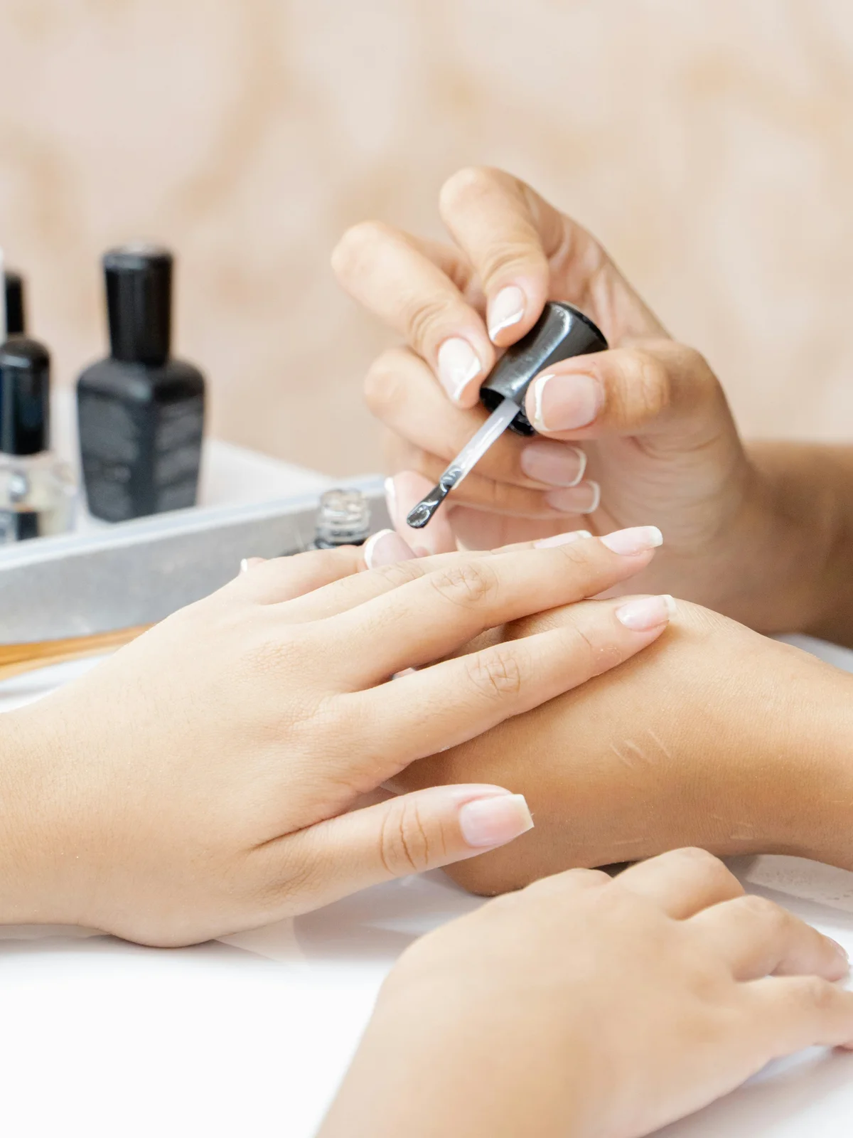 Close-up of a technician applying clear strengthening treatment to a client's nails in a beauty salon