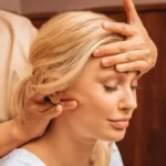 Close-up of a woman with her eyes closed as a therapist holds one hand on her forehead and massages her neck with the other hand during an Indian head massage