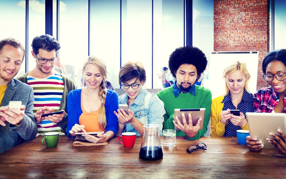Diverse groep mensen aan een tafel met smartphones en tablets, symbool voor online bijscholing van kappers en barbiers