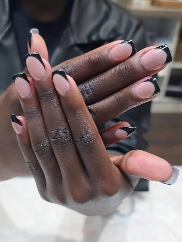 Vrouw in een nagelsalon die haar nude BIAB-manicure met zwarte verlengingen aan de camera laat zien