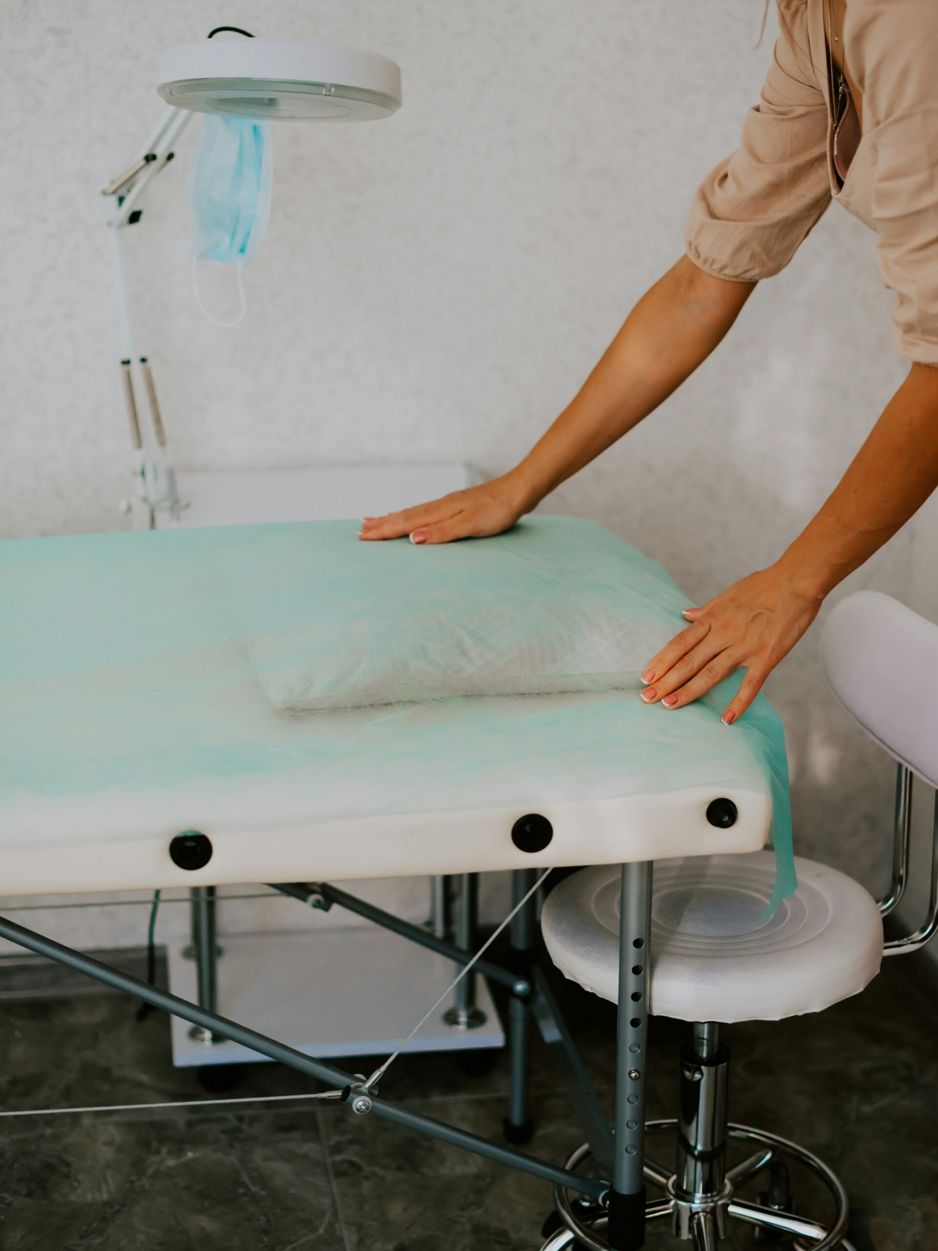 Een behandelkamer in een schoonheidssalon met een schone, hygiënische ruimte en een specialist die een schoon vel papier over een behandelbed legt