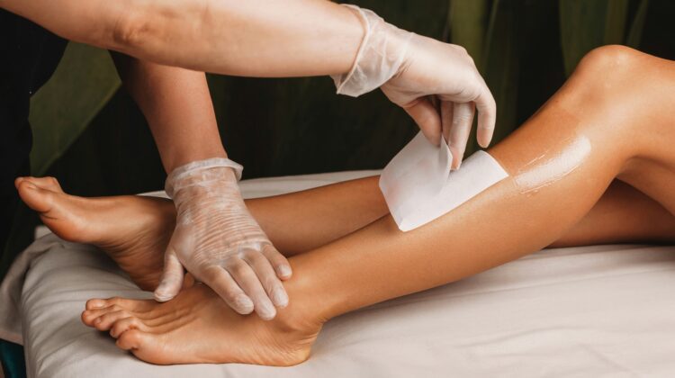 Close-up van een specialist die het onderbeen van een cliënt waxt in een lichte, schone salon