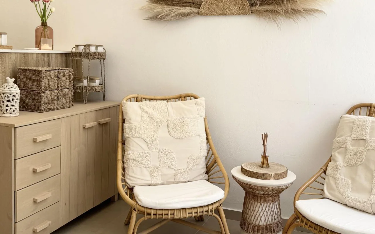 Een rustgevende wachtruimte met rotan fauteuils, getextureerde crèmekleurige kussens, een rieten bijzettafel met een geurstokje, gevlochten opbergmanden en gedroogd pampasgras aan de muur boven lichthouten kasten.