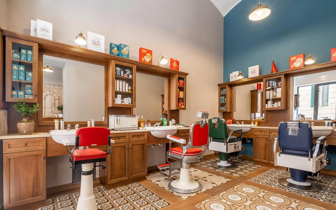 Een luxe traditionele barbershop met rijke houten kasten, vintage patronen op de vloertegels en professionele kappersstoelen in rood, groen en marineblauw. Traditionele verzorgingsproducten staan uitgestald op de schappen.