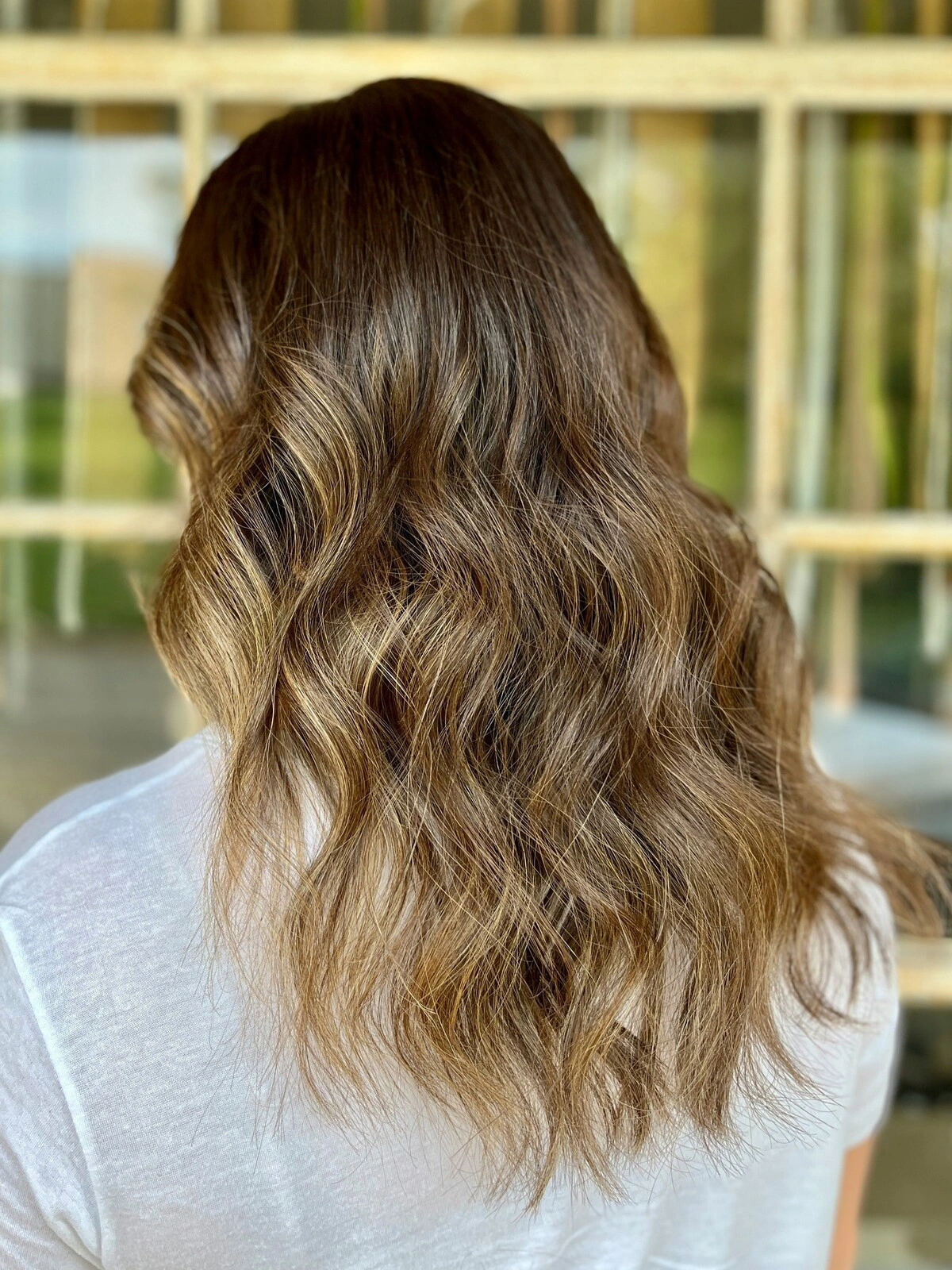Achteraanzicht van het hoofd van een vrouw met golvend balayage-haar waarbij het donkere haar overloopt in warme tinten