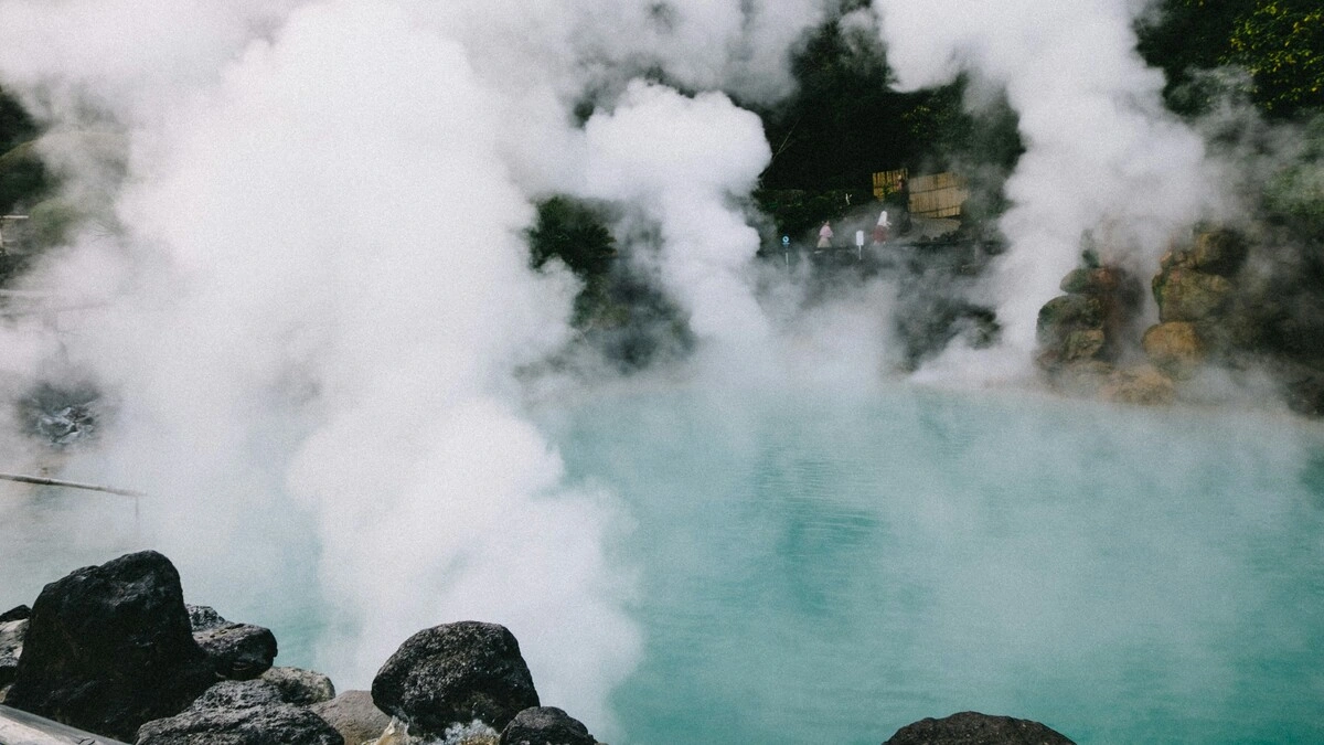 Breed beeld van warmwaterbronnen in Japan met stoomwolken die opstijgen uit een poel omringd door rotsen en groen