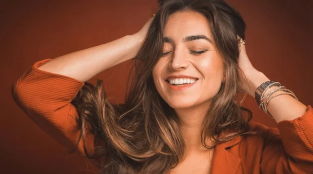 Close-up van een glimlachende vrouw met gesloten ogen die met haar handen door haar zachte, lange, donkerbruine haar gaat