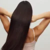 Achteraanzicht van een vrouw in een wit hemdje met haar armen omhoog, terwijl ze haar vingers door haar lange, glanzende donkerbruine haar haalt