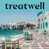 De boulevard van Klein Venetië in Mykonos-stad: witgekalkte huizen met kleurige houten balkons aan het water, daarachter de turkooizen Egeïsche Zee en op de voorgrond witte en petrolblauwe cafétafels op een geplaveid terras.