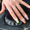 Een hand met de electric mani op de jog wheel van een Pioneer dj-speler, met neon french tips in dierenprint en swirls