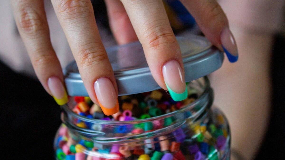 De hand van een vrouw met een French manicure met een transparante nude basis en gekleurde tips
