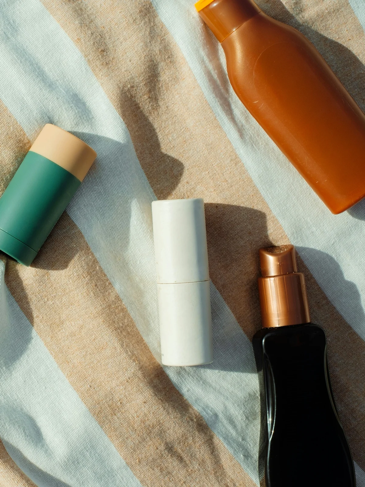 Bovenaanzicht van kleine flesjes en tubes verzorgingsproducten op een gestreepte katoenen doek