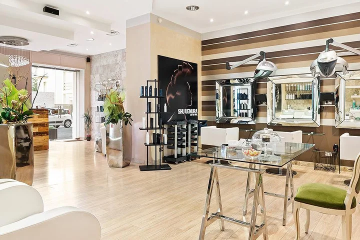 Elegante kappersstoelen bij Hair Queen in Cagliari met crème-en-bruin gestreepte muren en hoge zilverkleurige plantenbakken.
