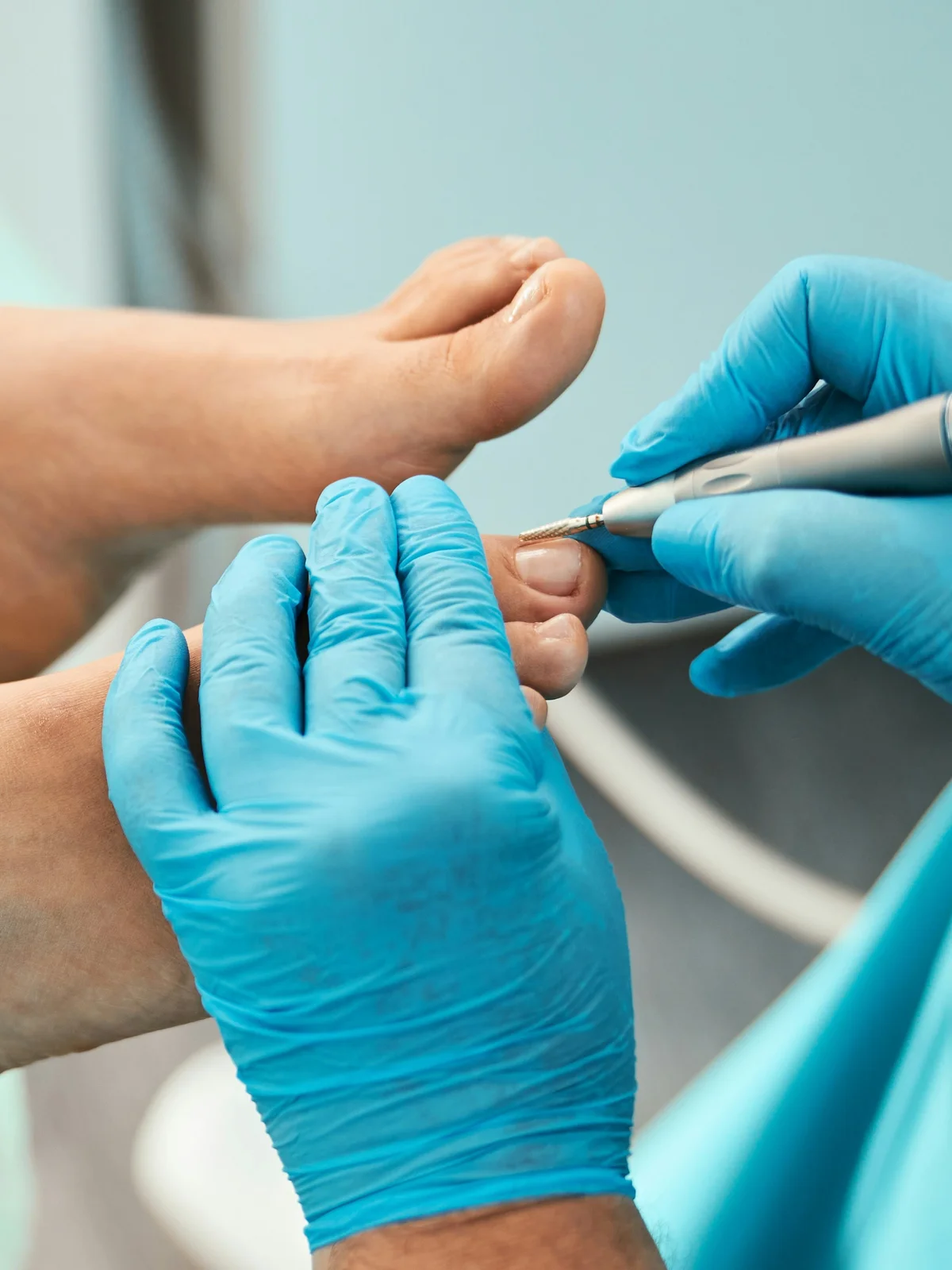 Close-up van een specialist met een handschoen aan die met een klein instrument de nagelriemen bij de tenen van een klant bijwerkt