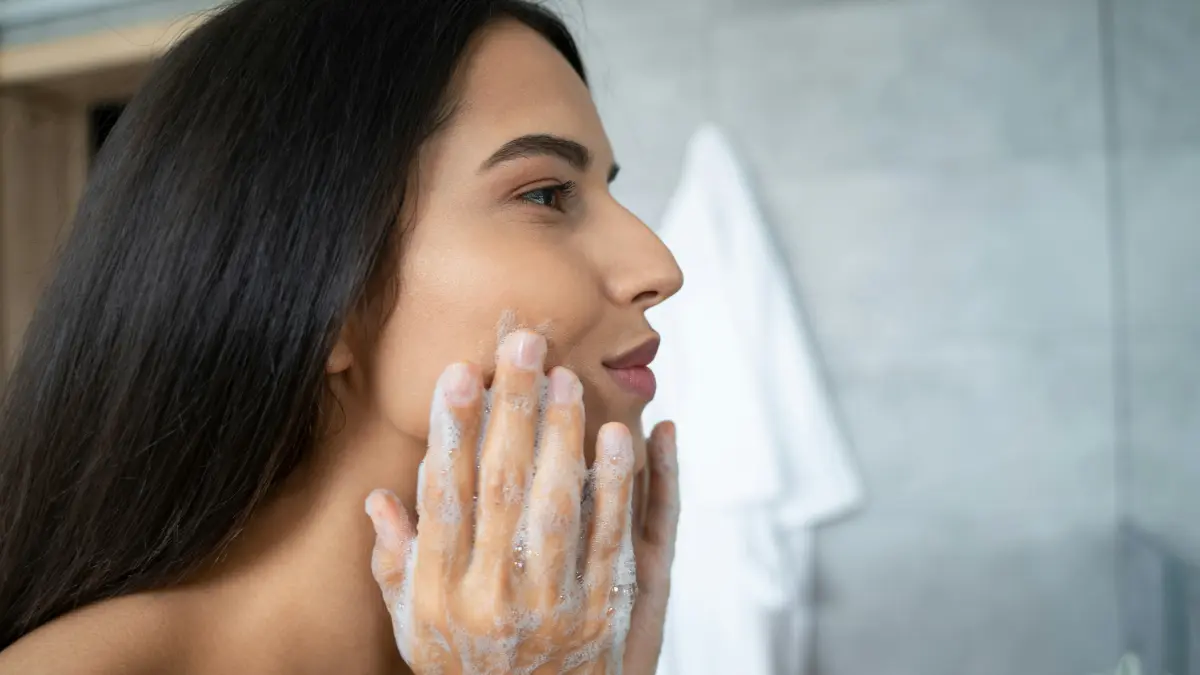Zijaanzicht van een vrouw die een cleanser in haar gezicht masseert terwijl ze over de wastafel gebogen staat