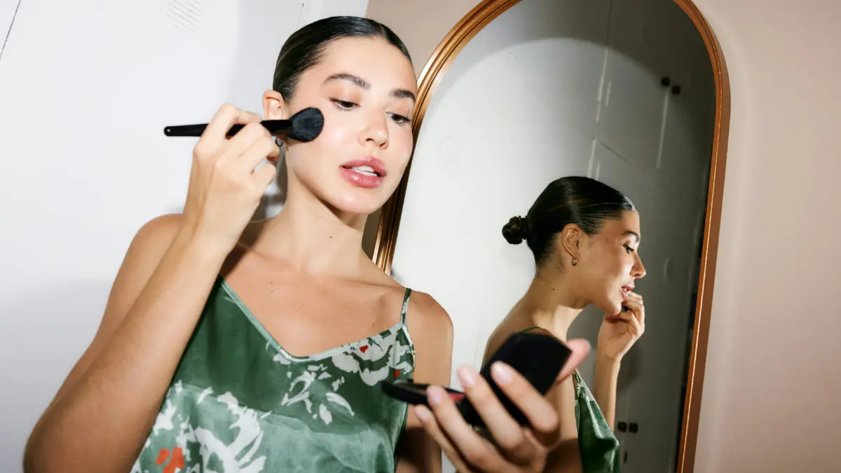 Een glamoureuze vrouw die klaar is om uit te gaan kijkt in een zakspiegeltje terwijl ze make-up aanbrengt met een kwast