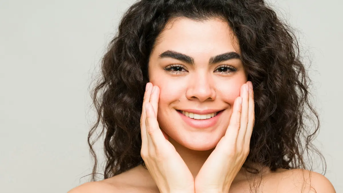 Een jonge vrouw met een gave huid en donker golvend haar lacht naar de camera
