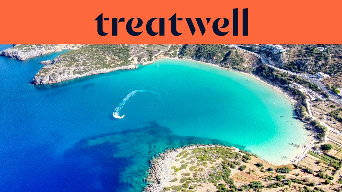 Luchtfoto van een turquoise Kretenzische baai, met een jetski die een witte curve door helder water trekt, een halvemaanvormig zandstrand en droge heuvels rond de kust, onder een koraaloranje banner met de tekst treatwell.
