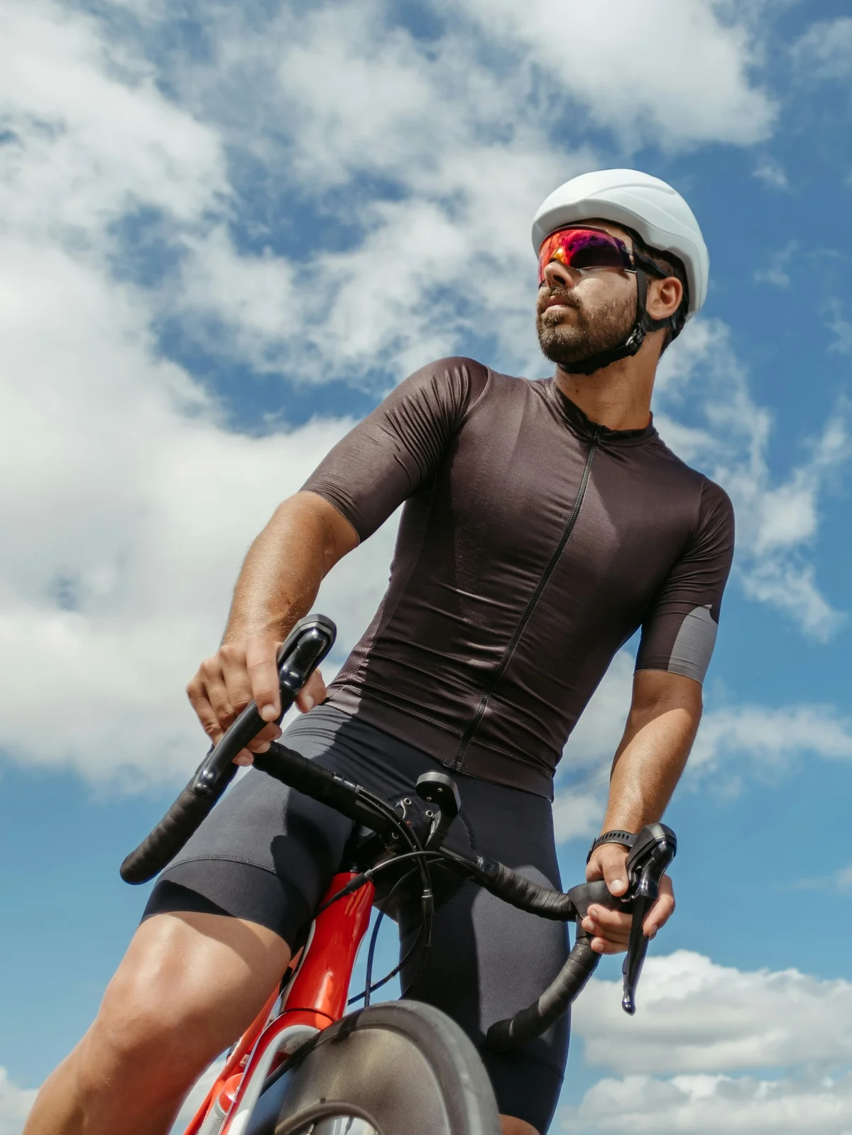 Van onderaf gefotografeerd: een wielrenner die op zijn fiets zit, stopt om om zich heen te kijken onder een blauwe lucht met wolken