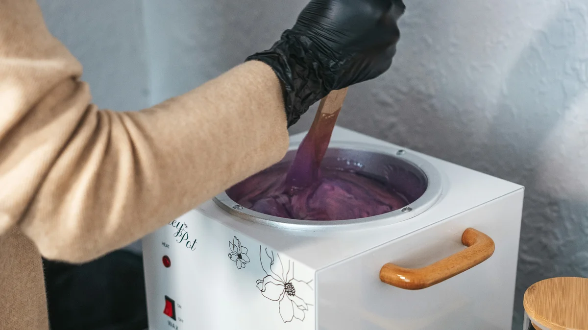 De hand van een specialist met een zwarte handschoen roert in een schoonheidssalon in een potje gesmolten wax