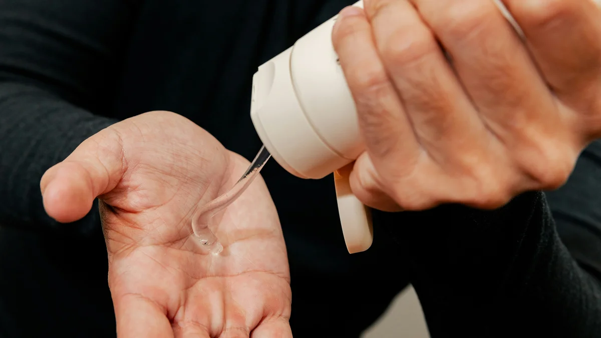 Close-up van de handen van een man die met één hand een witte tube hydraterende gel in zijn andere hand knijpt