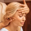 Close-up van een vrouw met haar ogen dicht terwijl een specialist tijdens een Indische hoofdmassage een hand op haar voorhoofd legt en met de andere hand haar nek masseert