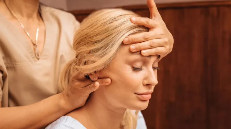 Close-up van een vrouw met haar ogen dicht terwijl een specialist tijdens een Indische hoofdmassage een hand op haar voorhoofd legt en met de andere hand haar nek masseert