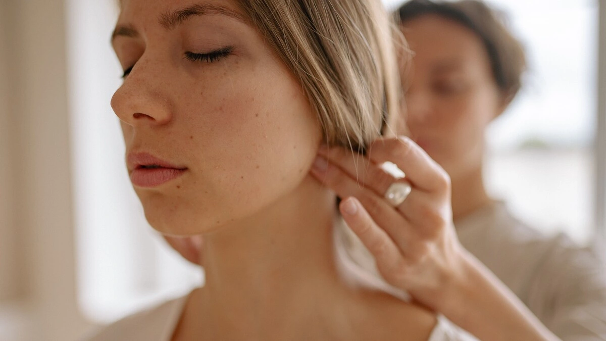 Close-up van een vrouw met haar ogen dicht terwijl een specialist tijdens een Indische hoofdmassage met de handen druk uitoefent op de basis van haar schedel